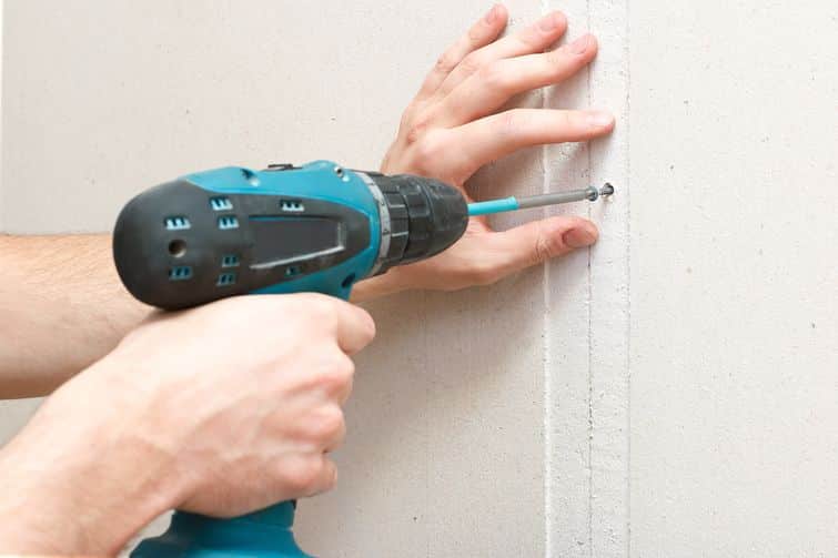 a man with a screwdriver in his hand fastens drywall to the wall